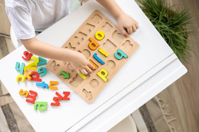 Vue de dessus d'un enfant manipulant des lettres en bois d'un puzzle, un outil clé de la méthode Montessori