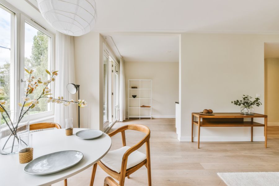 Un salon salle à manger lumineux au style de déco scandinave minimaliste avec mobilier en bois clair, murs beige et grandes fenêtres.