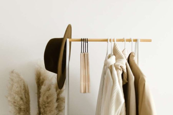 Un portant à vêtements minimaliste en métal blanc et bois met en valeur des tenues beiges suspendues et un chapeau élégant.